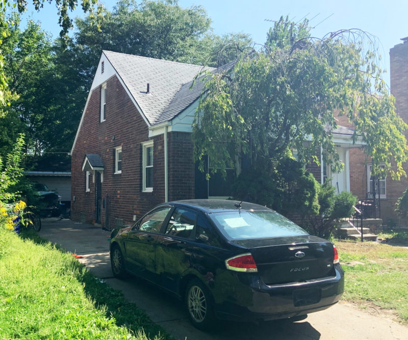 Corner view of a peaked brick home with a black sedan in the driveway