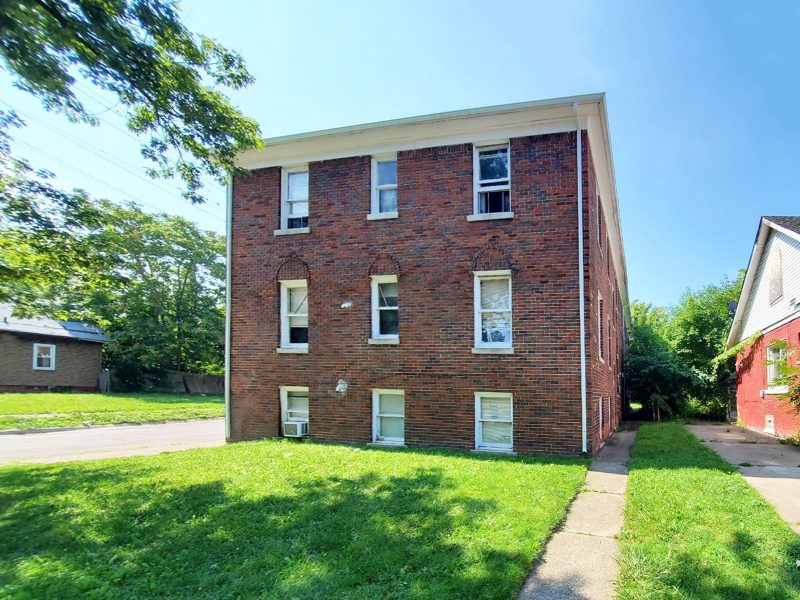 A side view of a 3-story brick 9-unit apartment buiding with white-trimmed windows and a green lawn.